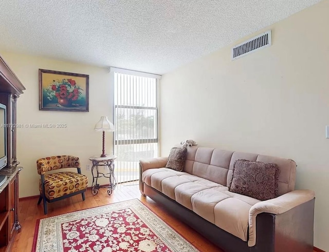 living area with expansive windows, a textured ceiling, wood finished floors, and visible vents