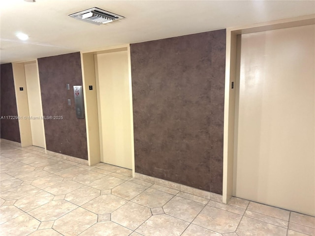 empty room featuring elevator, light tile patterned floors, and visible vents