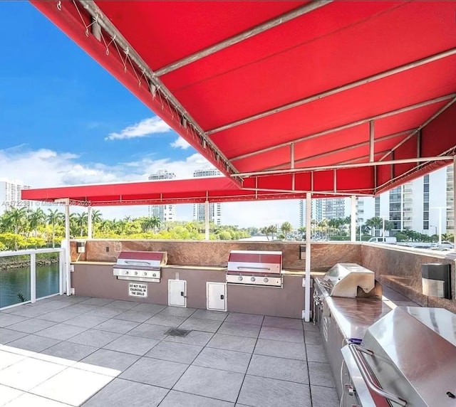 view of patio with grilling area, a water view, and an outdoor kitchen