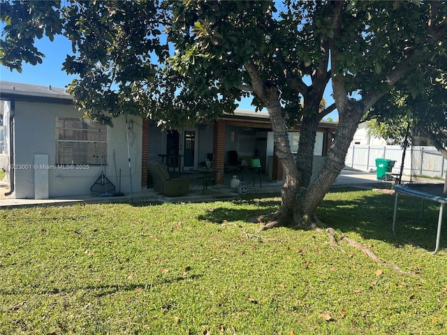 back of house featuring a patio, a trampoline, and a lawn