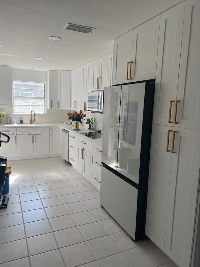 kitchen with sink, stainless steel dishwasher, fridge, light tile patterned flooring, and white cabinetry