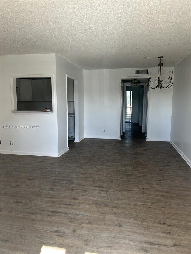 unfurnished room with dark hardwood / wood-style floors, a textured ceiling, and an inviting chandelier