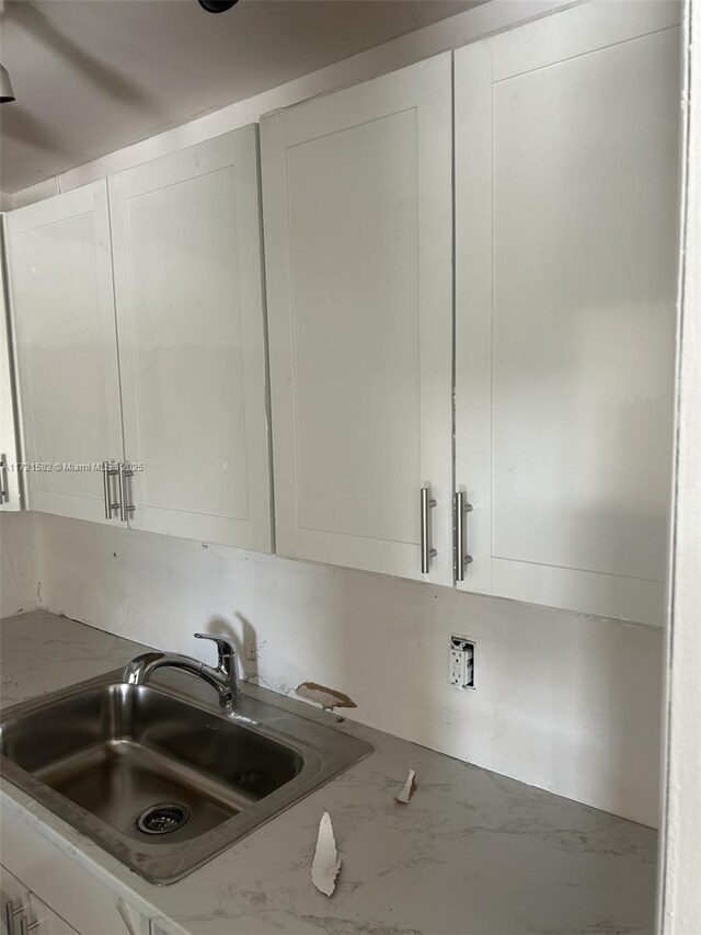 kitchen featuring white cabinets, light stone counters, and sink