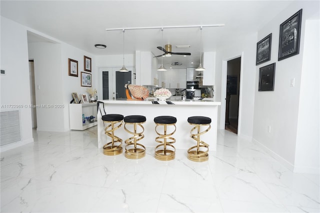 kitchen with visible vents, a peninsula, marble finish floor, a kitchen bar, and white cabinetry