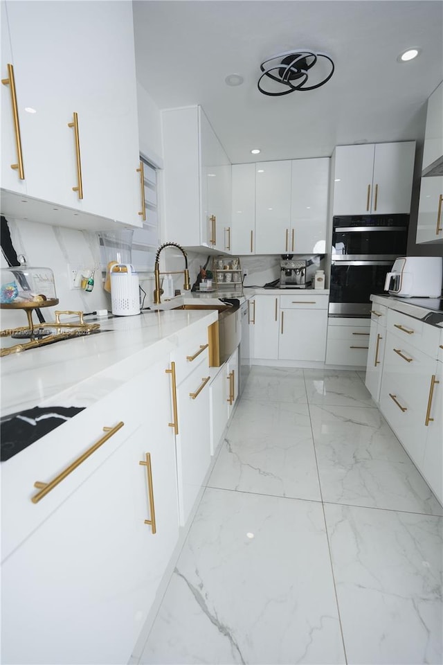 kitchen with modern cabinets, marble finish floor, stainless steel double oven, white cabinetry, and backsplash