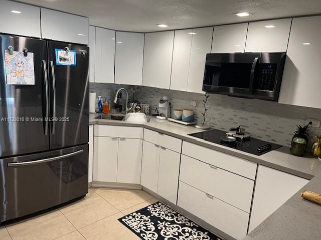 kitchen featuring white cabinets, light tile patterned floors, backsplash, and black appliances