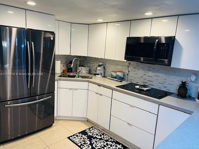 kitchen with light tile patterned flooring, white cabinetry, sink, fridge, and black electric cooktop