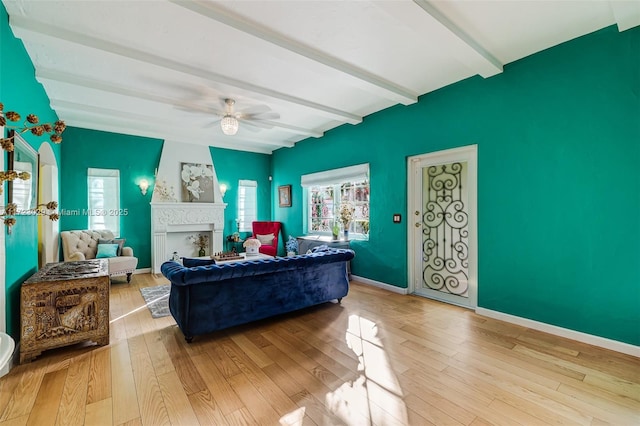 living room featuring beamed ceiling, light hardwood / wood-style floors, ceiling fan, and a fireplace