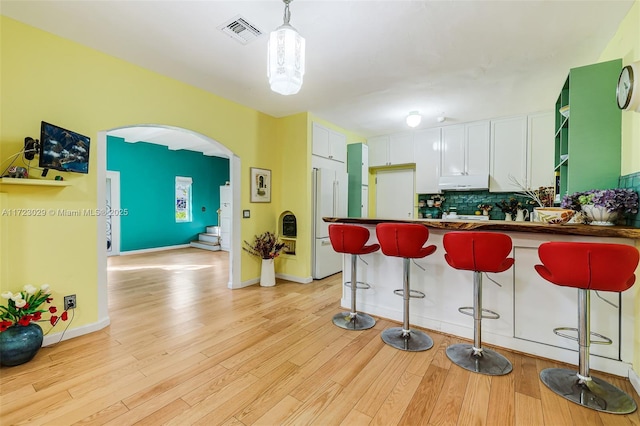 kitchen with backsplash, white cabinets, decorative light fixtures, high end fridge, and a breakfast bar area