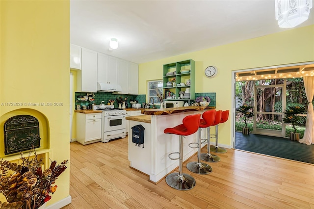 kitchen featuring white gas range, wood counters, kitchen peninsula, a breakfast bar area, and white cabinets