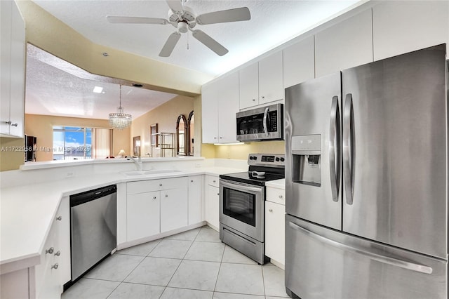 kitchen with ceiling fan with notable chandelier, stainless steel appliances, sink, pendant lighting, and white cabinets