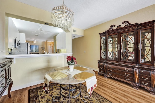 dining space featuring hardwood / wood-style flooring, ceiling fan with notable chandelier, and a textured ceiling