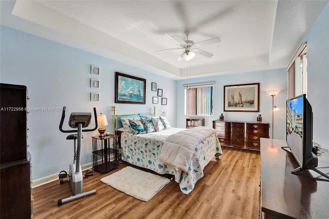 bedroom with ceiling fan, light hardwood / wood-style floors, and a raised ceiling