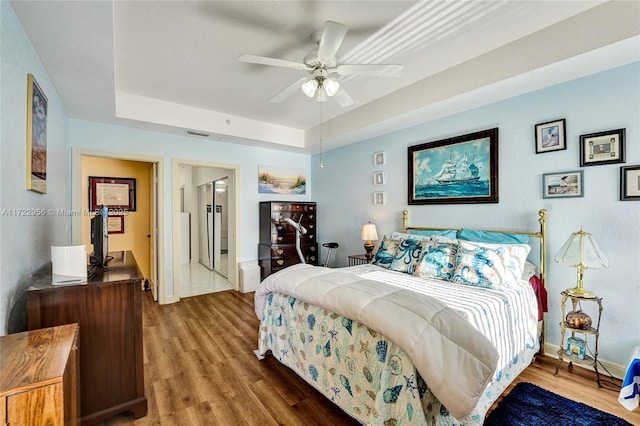 bedroom with ensuite bath, hardwood / wood-style flooring, a raised ceiling, and ceiling fan