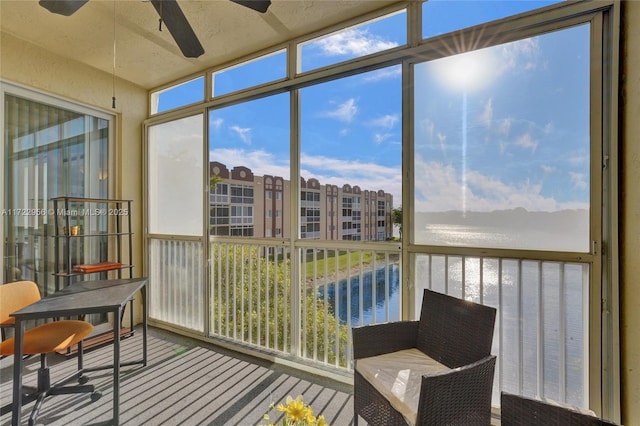 sunroom featuring ceiling fan and a water view