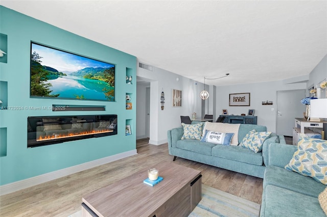 living area with a glass covered fireplace, wood finished floors, visible vents, and baseboards