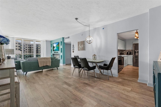 dining space with visible vents, an inviting chandelier, expansive windows, a textured ceiling, and light wood-type flooring