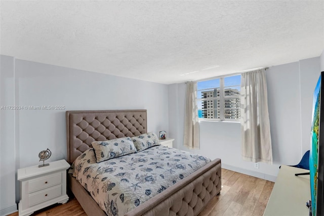 bedroom featuring a textured ceiling, light wood-type flooring, and baseboards