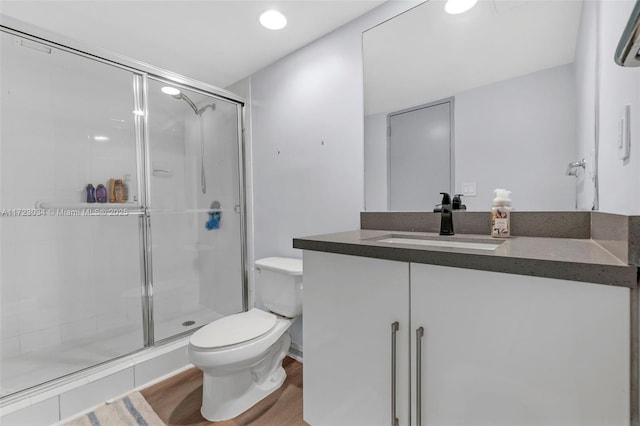 bathroom with toilet, a stall shower, wood finished floors, and vanity