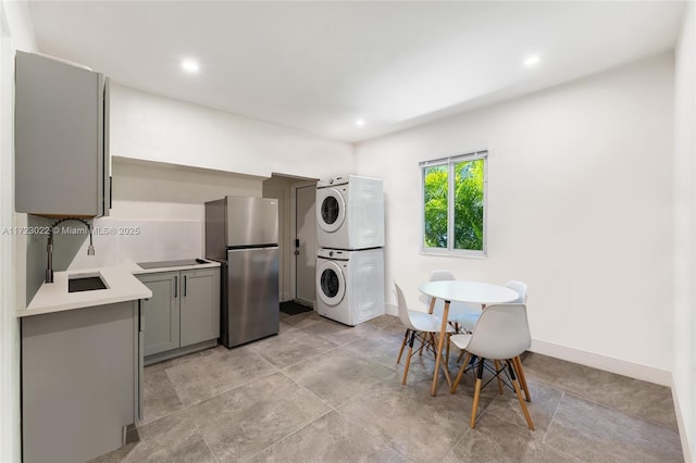 kitchen featuring sink, stainless steel refrigerator, stacked washer and clothes dryer, and gray cabinetry