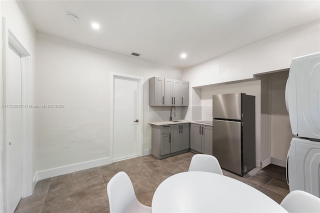 kitchen featuring stainless steel refrigerator, stacked washer / dryer, gray cabinetry, and sink