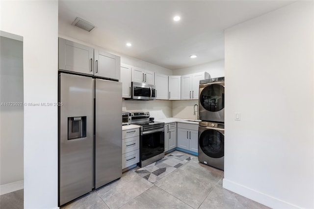 kitchen featuring gray cabinetry, sink, stacked washer and dryer, and appliances with stainless steel finishes