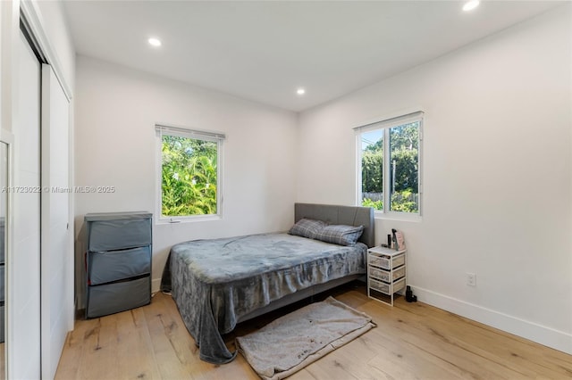 bedroom with a closet, light hardwood / wood-style floors, and multiple windows