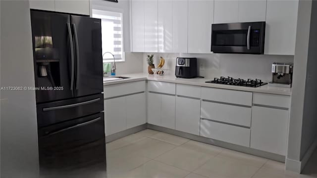 kitchen featuring tasteful backsplash, sink, black appliances, light tile patterned floors, and white cabinets