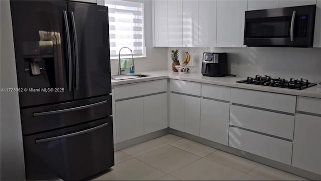 kitchen with sink, light tile patterned floors, black gas cooktop, stainless steel fridge, and white cabinets