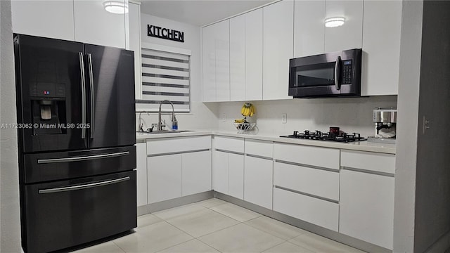 kitchen featuring black appliances, white cabinetry, sink, and light tile patterned floors