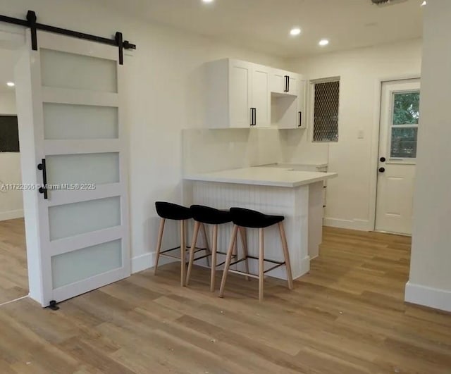 kitchen featuring white cabinetry, light wood-type flooring, a kitchen bar, and a barn door