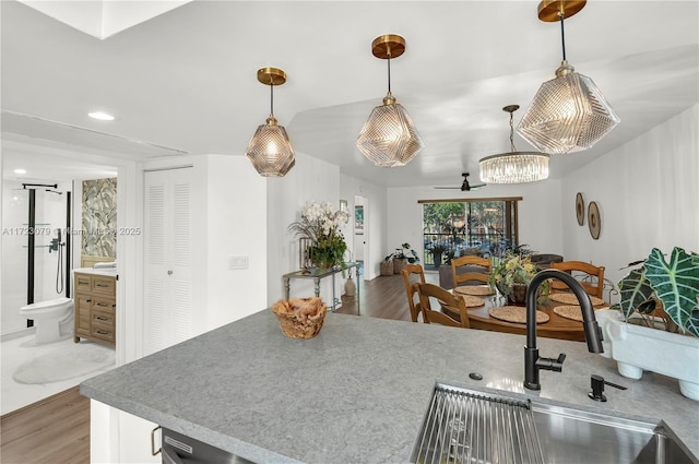 kitchen with pendant lighting, ceiling fan with notable chandelier, sink, and hardwood / wood-style floors