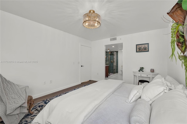 bedroom with ensuite bath, wood-type flooring, and a chandelier