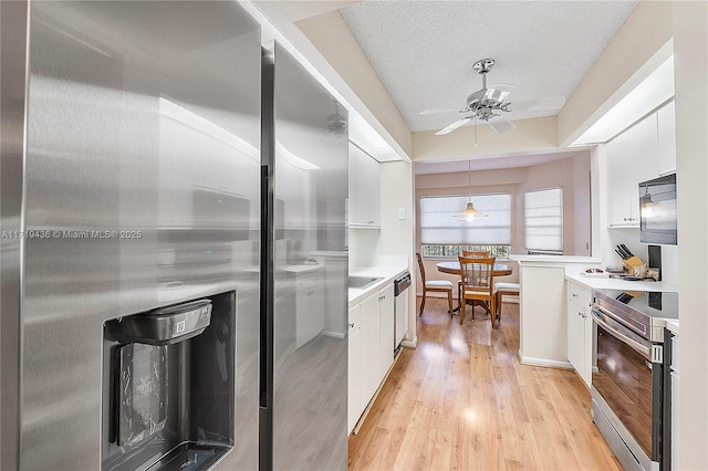 kitchen featuring a textured ceiling, white cabinetry, stainless steel appliances, and hanging light fixtures