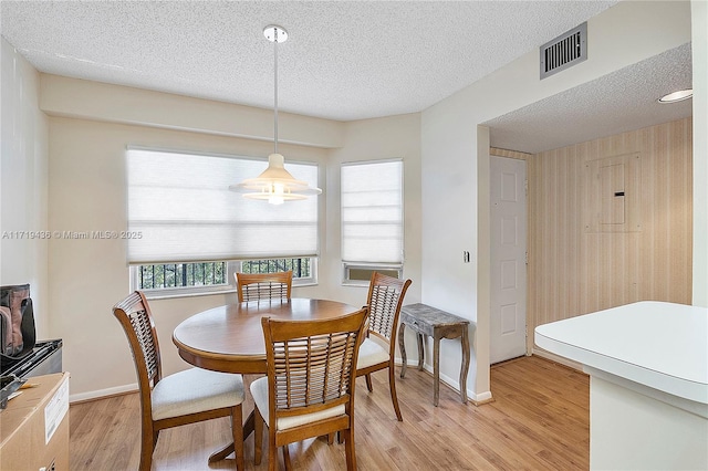 dining room with light wood-type flooring, a textured ceiling, and electric panel