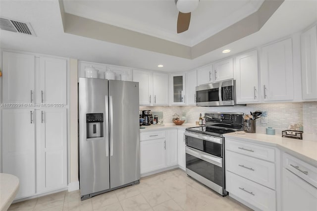 kitchen with white cabinets, appliances with stainless steel finishes, a tray ceiling, and decorative backsplash