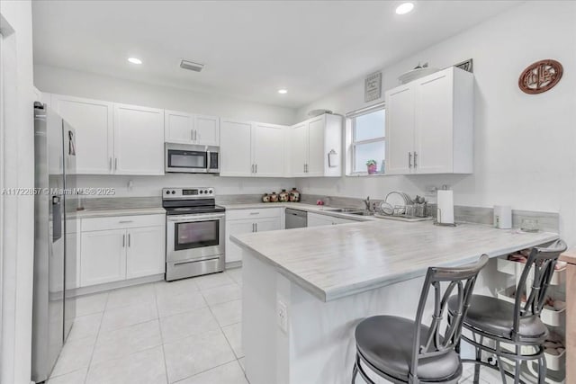 kitchen featuring a kitchen bar, kitchen peninsula, white cabinetry, and appliances with stainless steel finishes