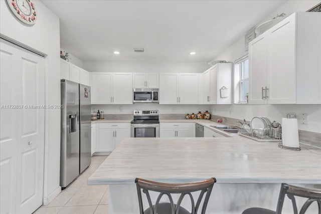 kitchen featuring a breakfast bar, kitchen peninsula, light tile patterned floors, appliances with stainless steel finishes, and white cabinetry