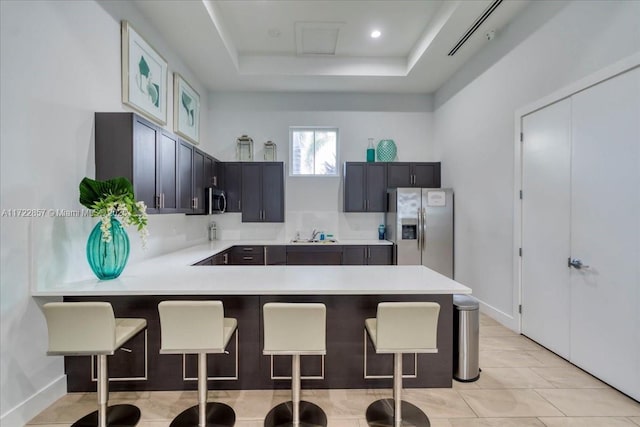 kitchen with sink, a tray ceiling, a kitchen bar, kitchen peninsula, and stainless steel appliances