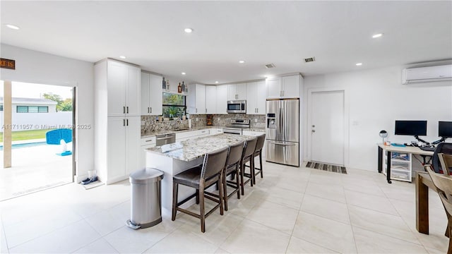 kitchen featuring a kitchen bar, appliances with stainless steel finishes, a kitchen island, a wall unit AC, and white cabinetry