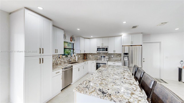 kitchen with decorative backsplash, light stone countertops, white cabinetry, and appliances with stainless steel finishes