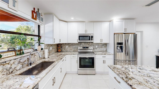 kitchen featuring backsplash, sink, appliances with stainless steel finishes, light tile patterned flooring, and white cabinetry