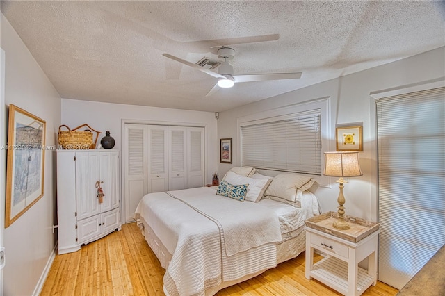 bedroom featuring light wood finished floors, a closet, visible vents, a ceiling fan, and a textured ceiling