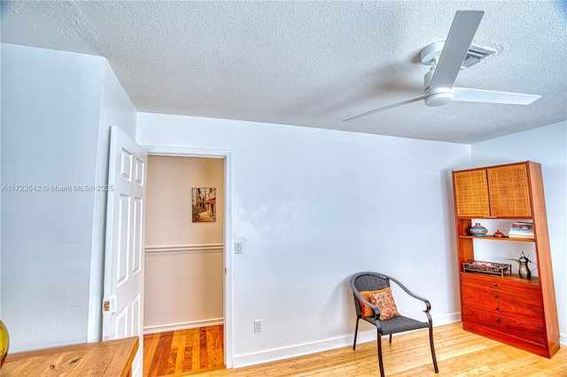 sitting room with light wood-style floors, ceiling fan, baseboards, and a textured ceiling