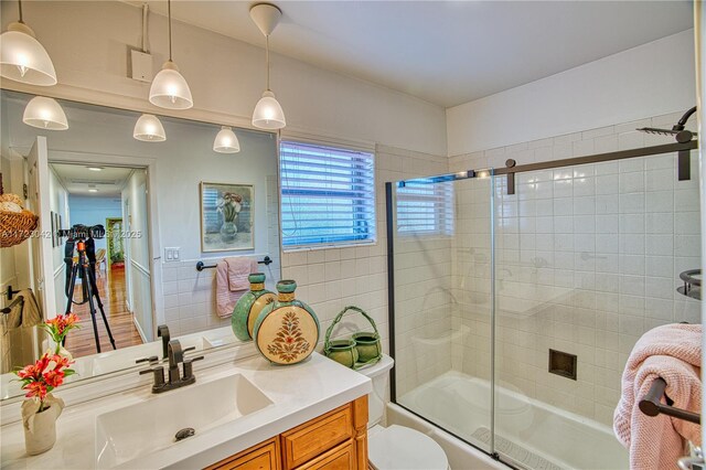 bathroom with toilet, bath / shower combo with glass door, tile walls, and vanity