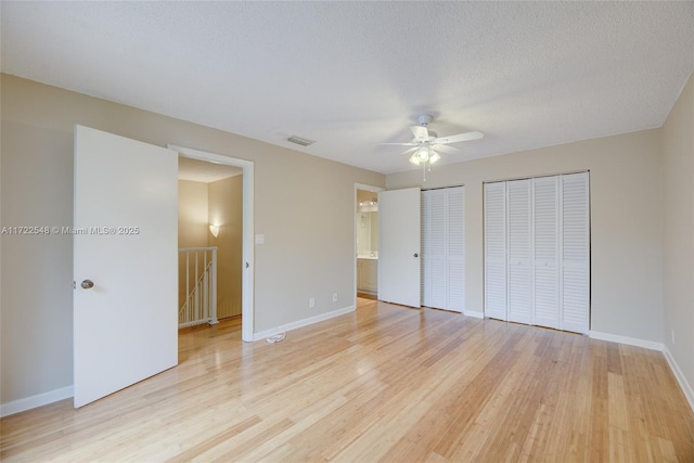 unfurnished bedroom with light wood-type flooring, two closets, ceiling fan, and ensuite bathroom