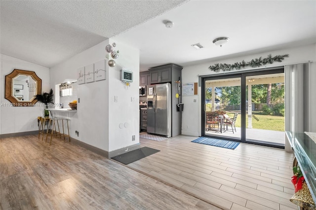 kitchen featuring kitchen peninsula, light wood-type flooring, a textured ceiling, stainless steel appliances, and lofted ceiling