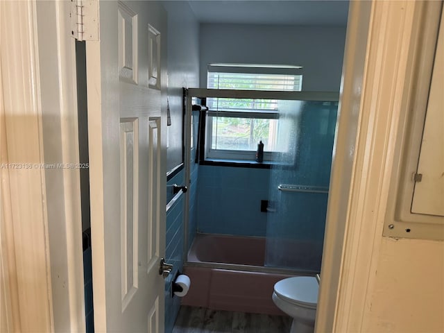 bathroom featuring hardwood / wood-style flooring, toilet, and shower / bath combination with glass door