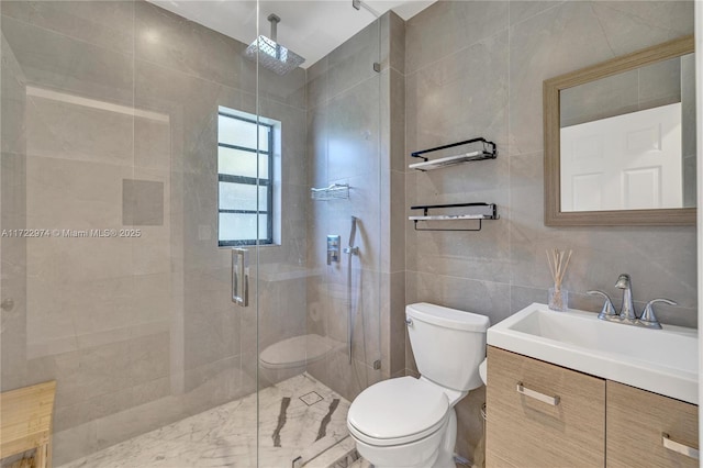 bathroom with a shower with door, vanity, tile walls, and toilet