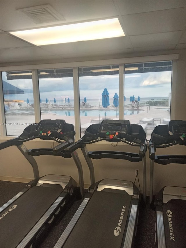 exercise room with a drop ceiling and a water view